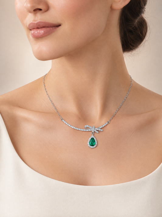 Emerald Bow Heart Pendant Necklace worn at the throat, rhodium-plated sterling silver with green pear-cut stone